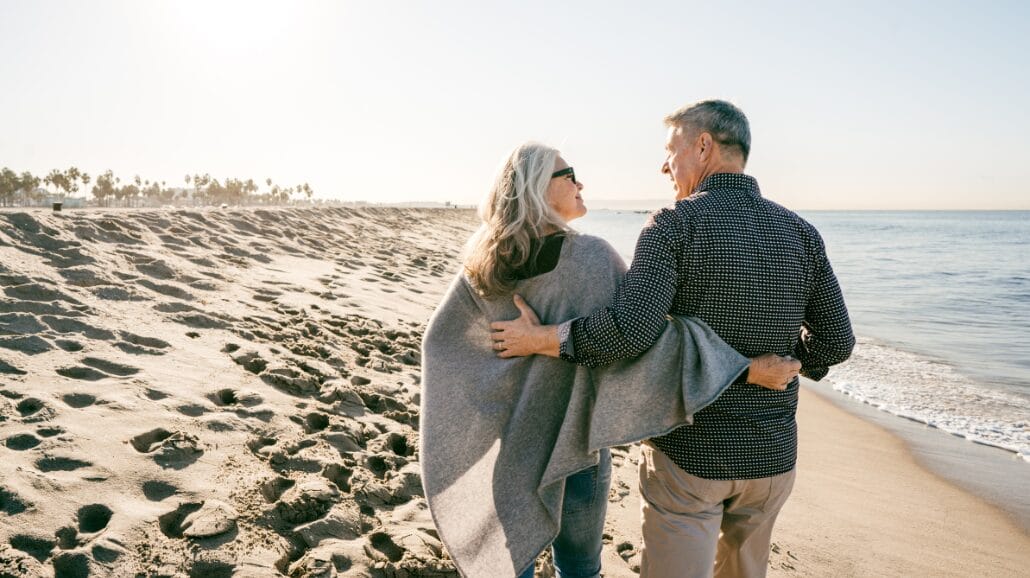 Senior couple walking down the beach at sunset