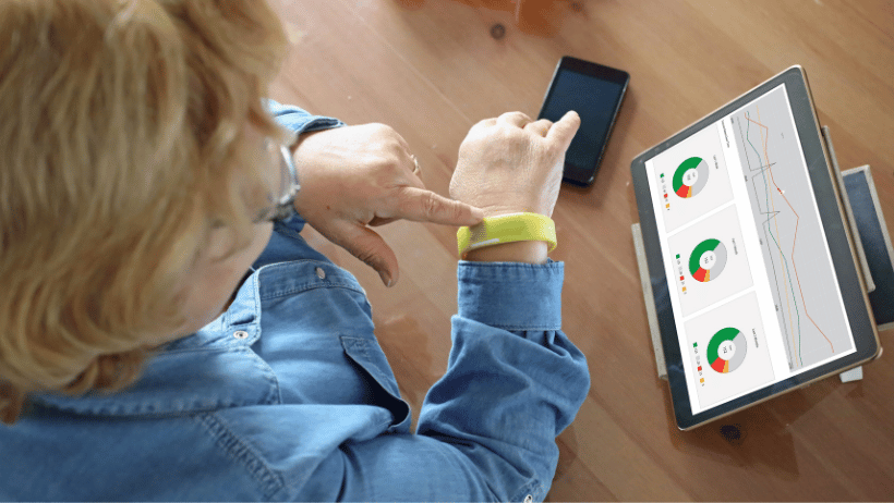 Senior touching a wrist wearable while looking at health stats on a tablet