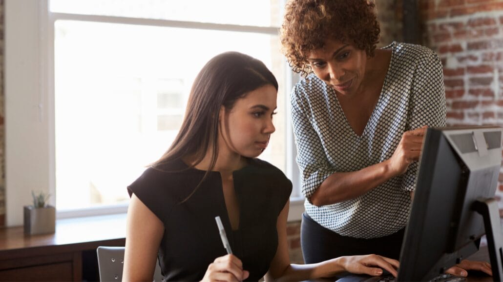 A professional taking training courses with a mentor helping her at a computer