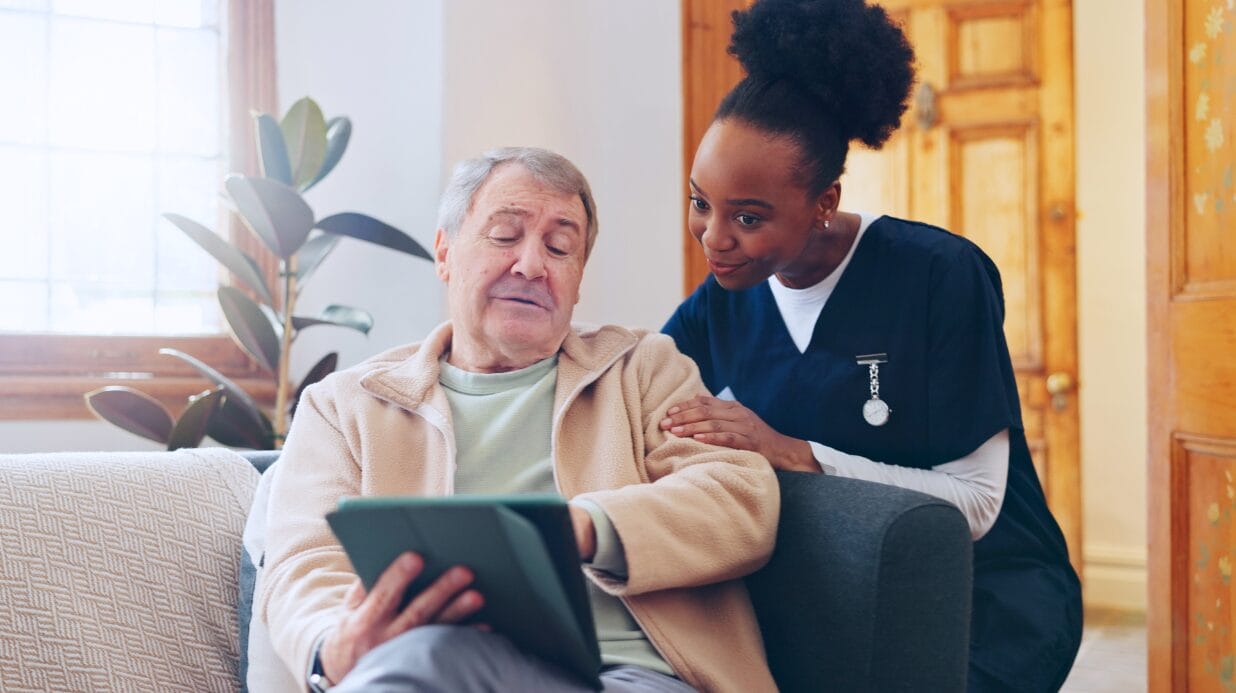 Caregiver assisting an elderly man with a tablet