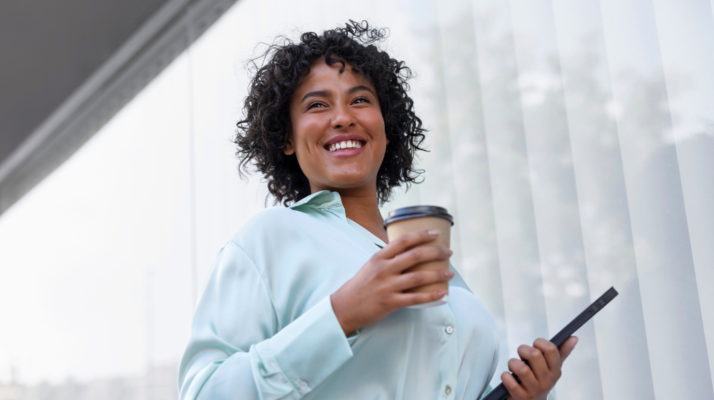 Confident female walking outside with coffee and tablet